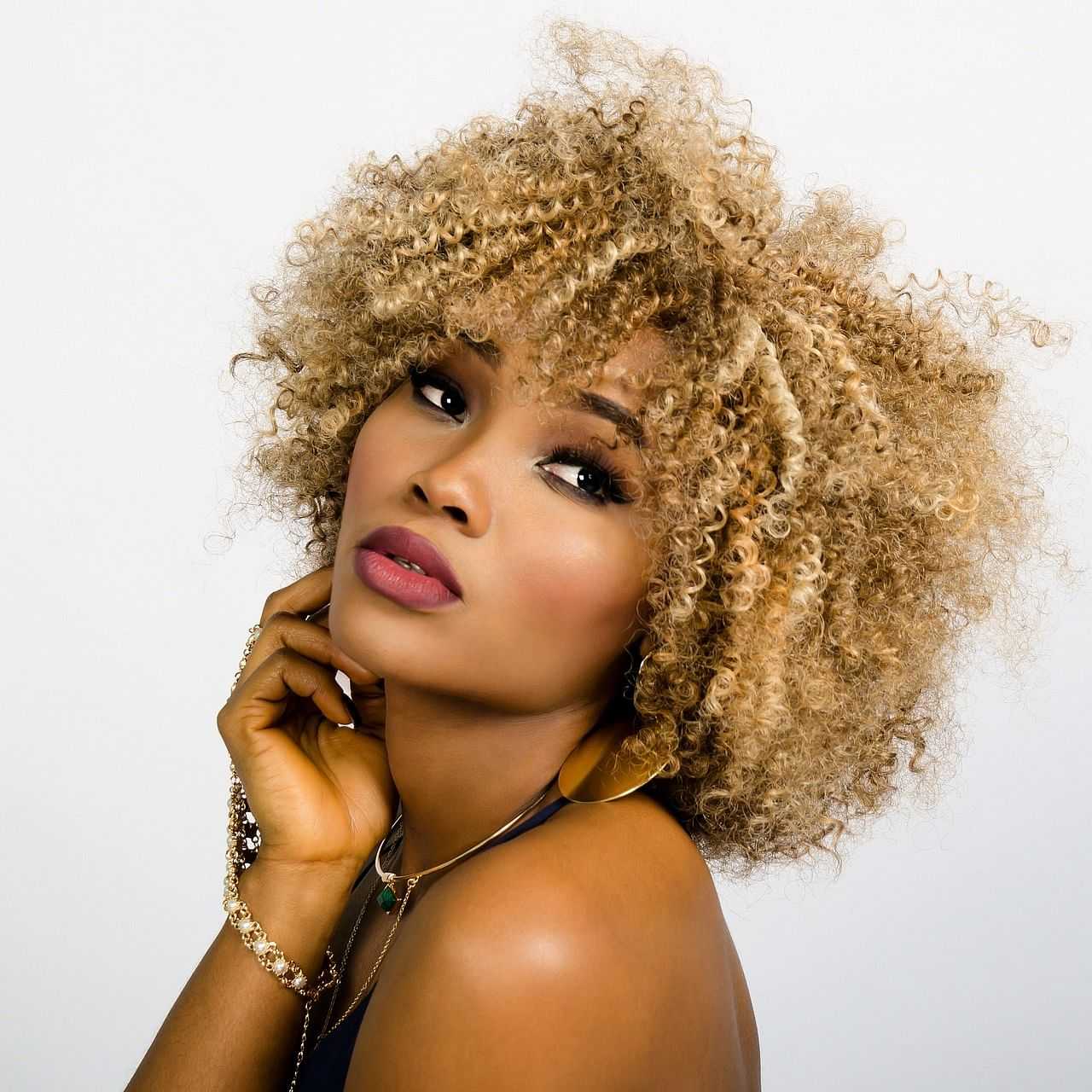 Woman with curly hair posing thoughtfully against a white backdrop.